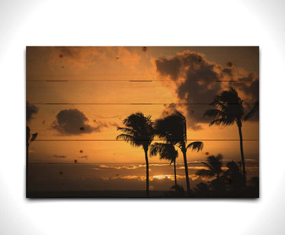 A photo of palm trees in Maui silhouetted by the setting sun, with the sea in the background. Printed on a wood pallet.