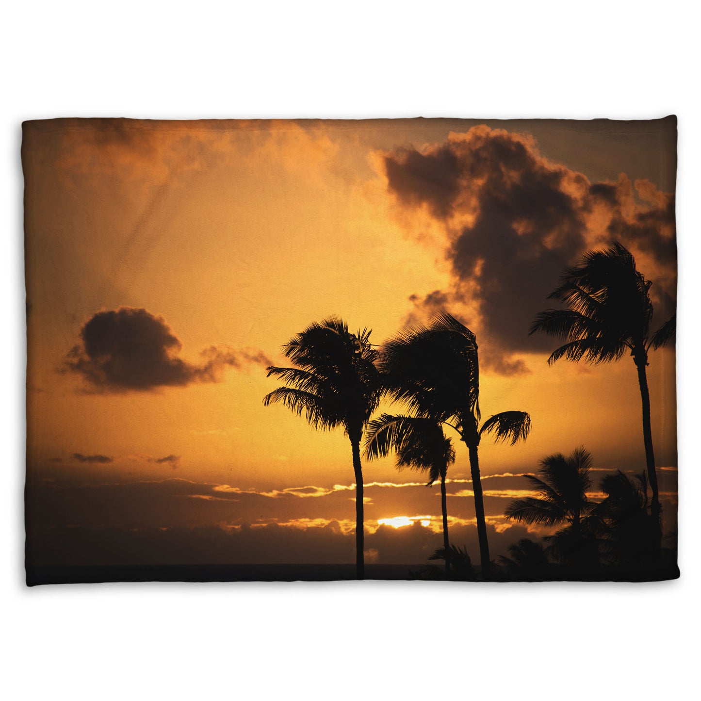 A coral fleece blanket designed with a photo of palm trees in Maui silhouetted by the setting sun, with the sea in the background.