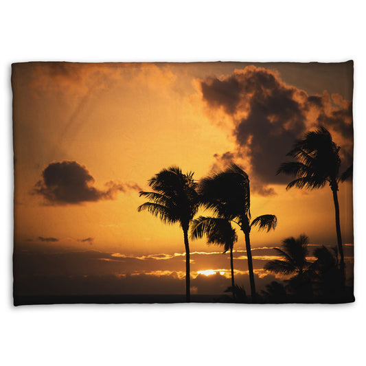 A coral fleece blanket designed with a photo of palm trees in Maui silhouetted by the setting sun, with the sea in the background.