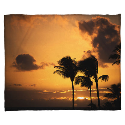 A coral fleece blanket designed with a photo of palm trees in Maui silhouetted by the setting sun, with the sea in the background.