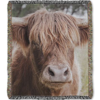 A woven throw blanket designed with a closeup portrait photograph of a fluffy highland cow.