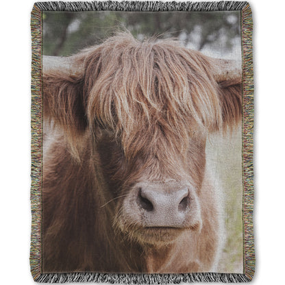A woven throw blanket designed with a closeup portrait photograph of a fluffy highland cow.
