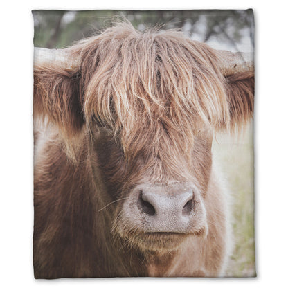 A fleece throw blanket designed with a closeup portrait photograph of a fluffy highland cow.
