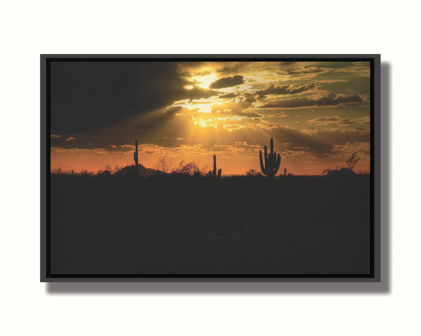 A photo of a sunset over the desert in Arizona, the landscape shadowed in black against the orange and yellow sky. Printed on canvas in a float frame.