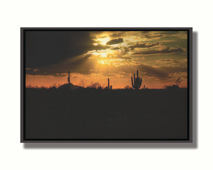 A photo of a sunset over the desert in Arizona, the landscape shadowed in black against the orange and yellow sky. Printed on canvas in a float frame.