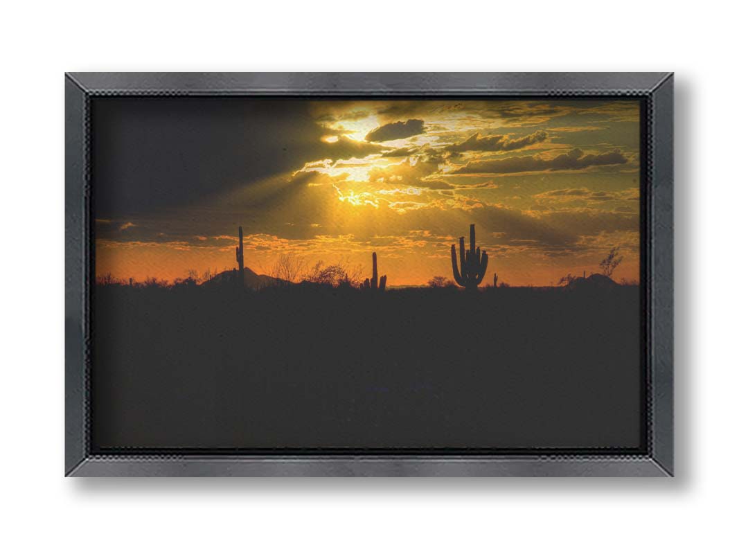 A photo of a sunset over the desert in Arizona, the landscape shadowed in black against the orange and yellow sky. Printed on canvas and framed.