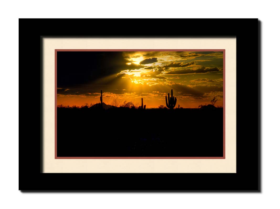 A photo of a sunset over the desert in Arizona, the landscape shadowed in black against the orange and yellow sky. Printed on paper, matted, and framed.