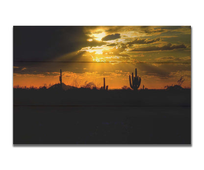 A photo of a sunset over the desert in Arizona, the landscape shadowed in black against the orange and yellow sky. Printed on a box board.