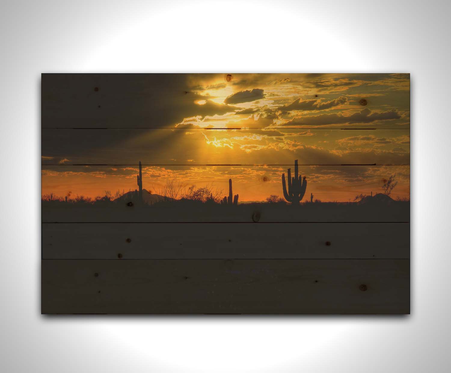 A photo of a sunset over the desert in Arizona, the landscape shadowed in black against the orange and yellow sky. Printed on a wood pallet.