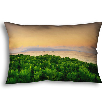 A throw pillow designed with a photo overlooking the sea from Kaanapali beach in Hawaii. Green plants fill the foreground, and boats sail on the water in the distance against a gentle orange sky and purple clouds. 