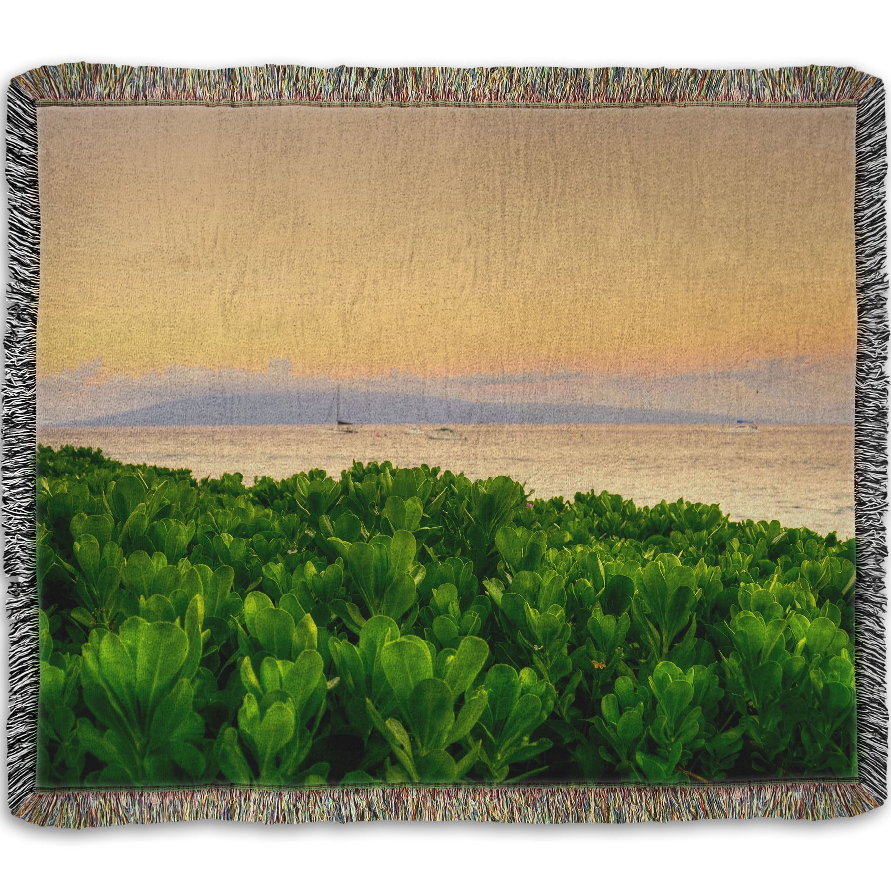 A woven throw blanket designed with a photo overlooking the sea from Kaanapali beach in Hawaii. Green plants fill the foreground, and boats sail on the water in the distance against a gentle orange sky and purple clouds. 