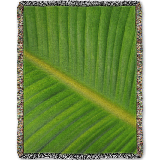 A woven throw blanket designed with a closeup photo of a leaf of a bird of paradise palm, showing all the detail of the midrib and veins of the leaf.