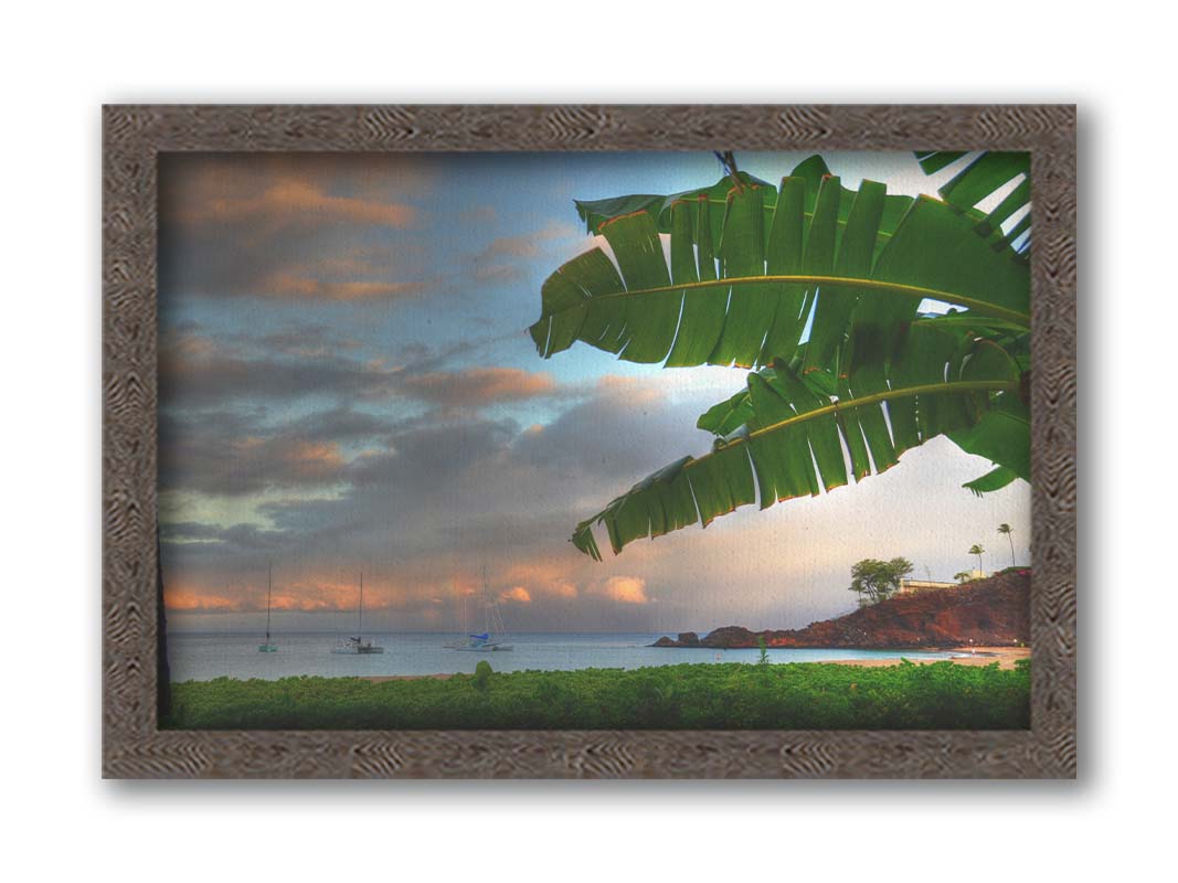 A photo of Ka'anapali beach in Hawai'i. Boats can be seen sailing on the ocean, and bright green plants grow in the foreground alongside a palm. Printed on canvas and framed.