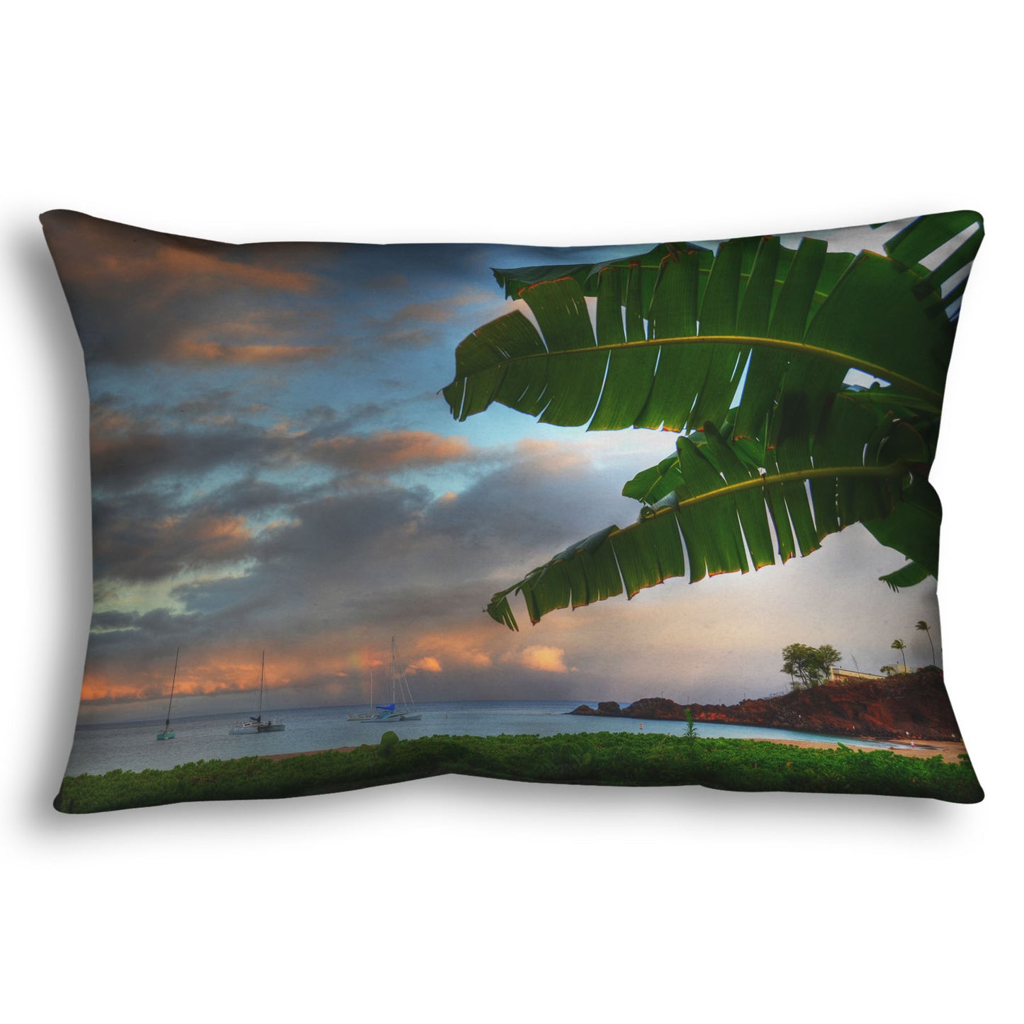 A throw pillow designed with a photo of Ka'anapali beach in Hawai'i. Boats can be seen sailing on the ocean, and bright green plants grow in the foreground alongside a palm.