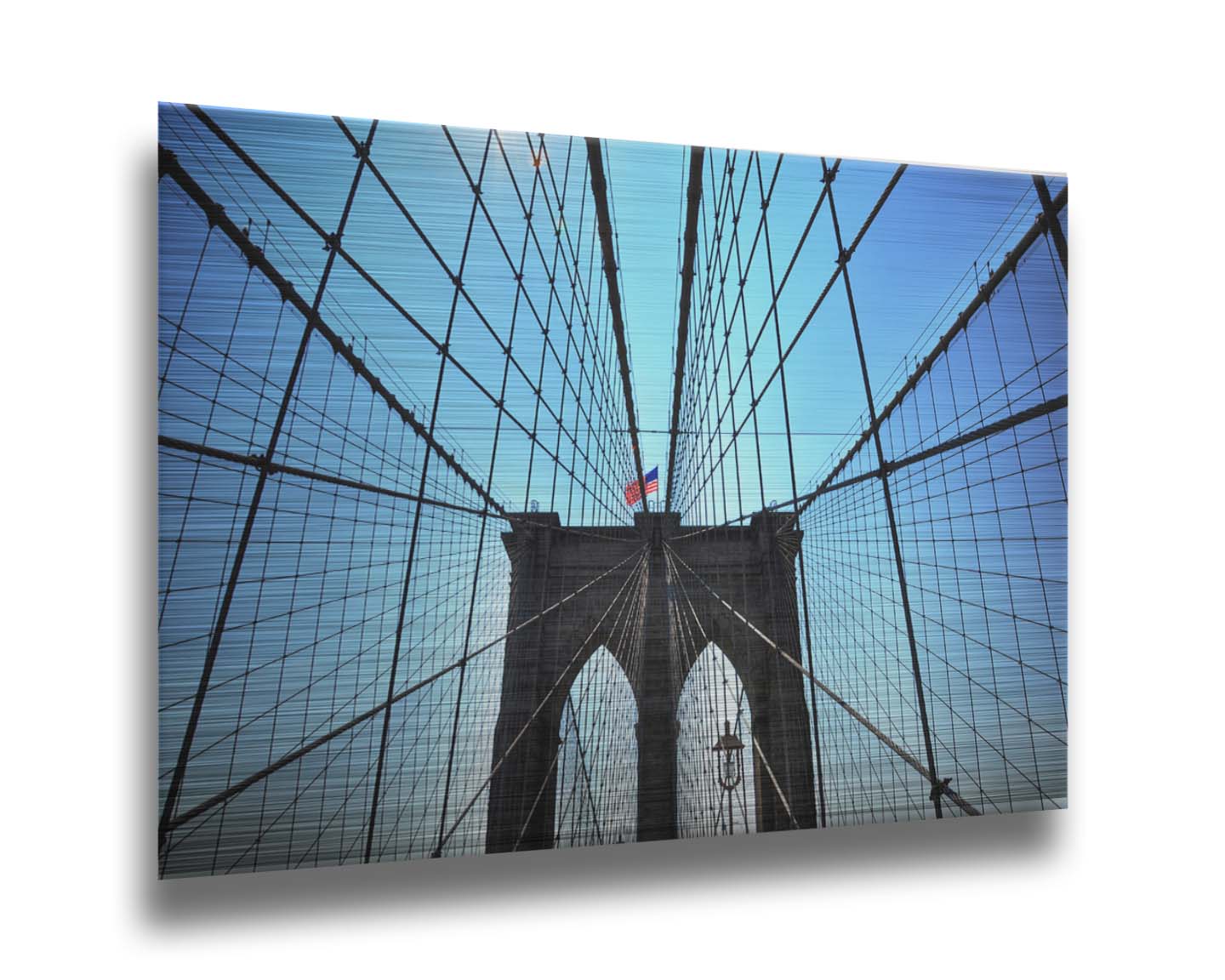 A photo of the Brooklyn Bridge, looking up the suspender cables at one of the towers, topped with an American flag. Printed on metal.