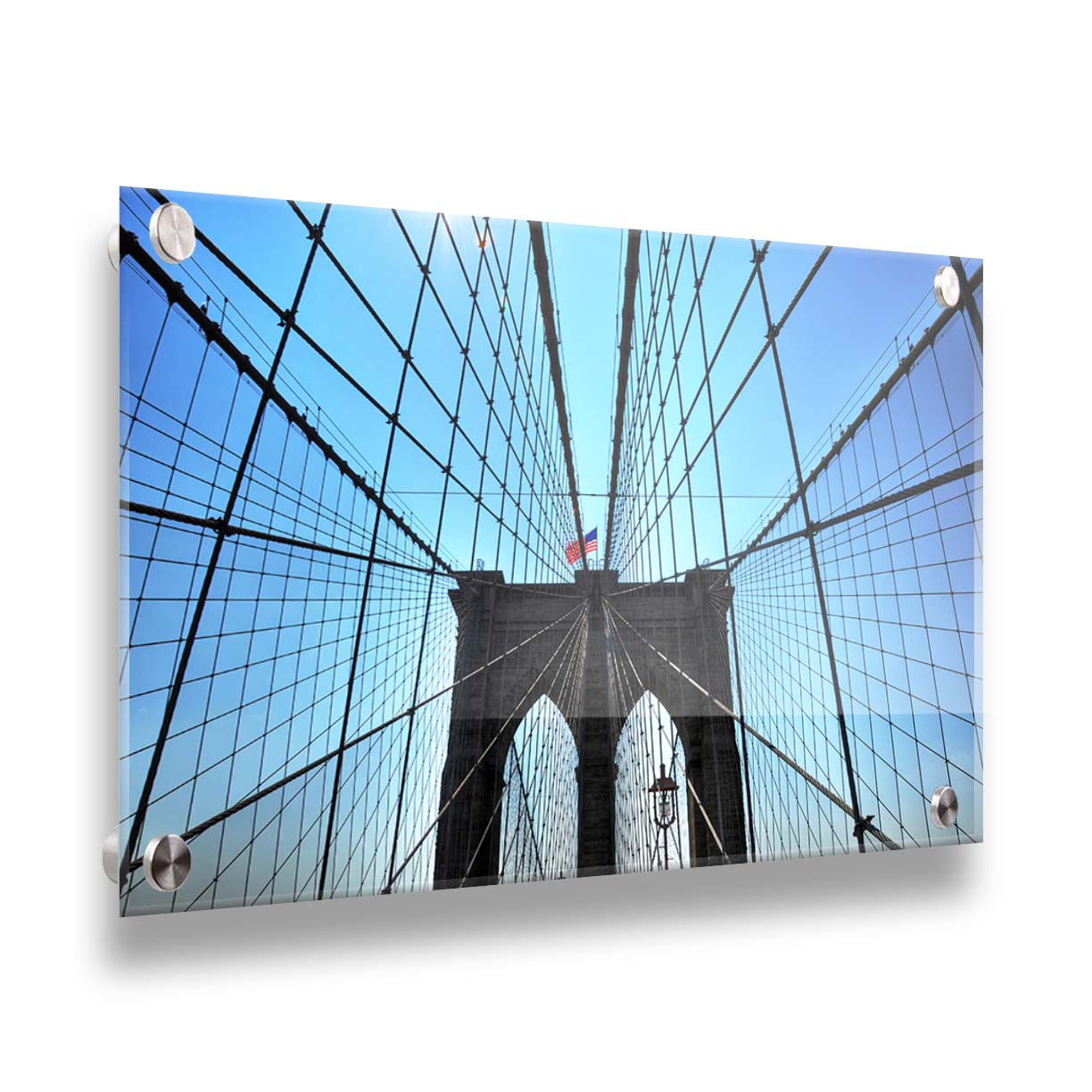 A photo of the Brooklyn Bridge, looking up the suspender cables at one of the towers, topped with an American flag. Printed on acrylic.