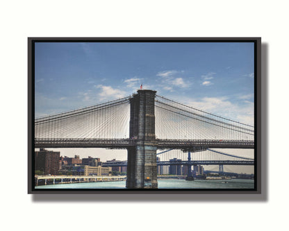 A photo of a side view of the Brooklyn Bridge against a blue sky. Printed on canvas in a float frame.