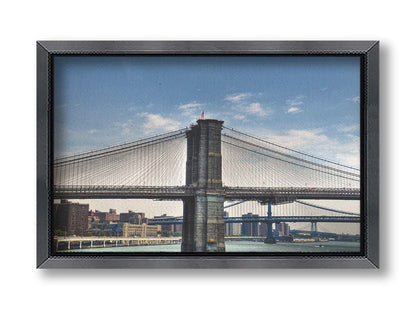 A photo of a side view of the Brooklyn Bridge against a blue sky. Printed on canvas and framed.