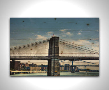 A photo of a side view of the Brooklyn Bridge against a blue sky. Printed on a wood pallet.