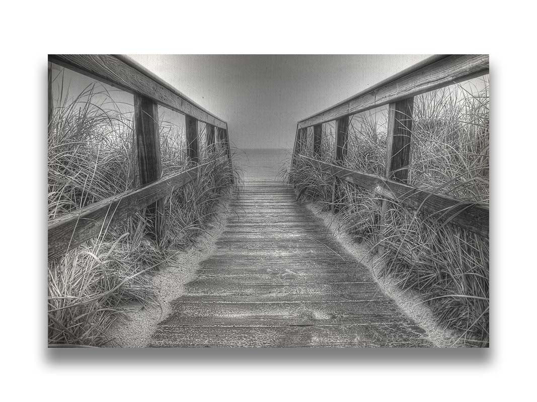 A grayscale photo looking down a wooden railed path on the beach at Cape Cod. Printed on canvas.