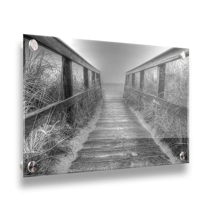 A grayscale photo looking down a wooden railed path on the beach at Cape Cod. Printed on acrylic.