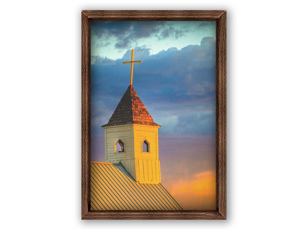 A photo of a cross-topped church at sunset, the sky gradiating from blue to purple to orange. Printed on canvas and framed.