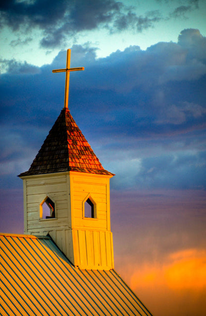 A photo of a cross-topped church at sunset, the sky gradating from blue to purple to orange. 
