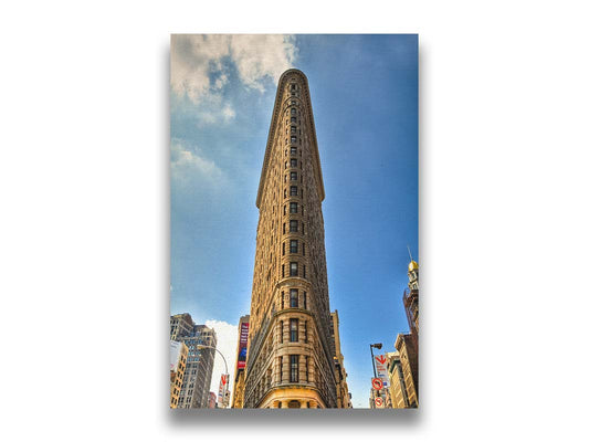 A photo of the Flatiron Building in New York City, New York. Its iconic triangular shape is captures against a bright blue sky. Printed on canvas.