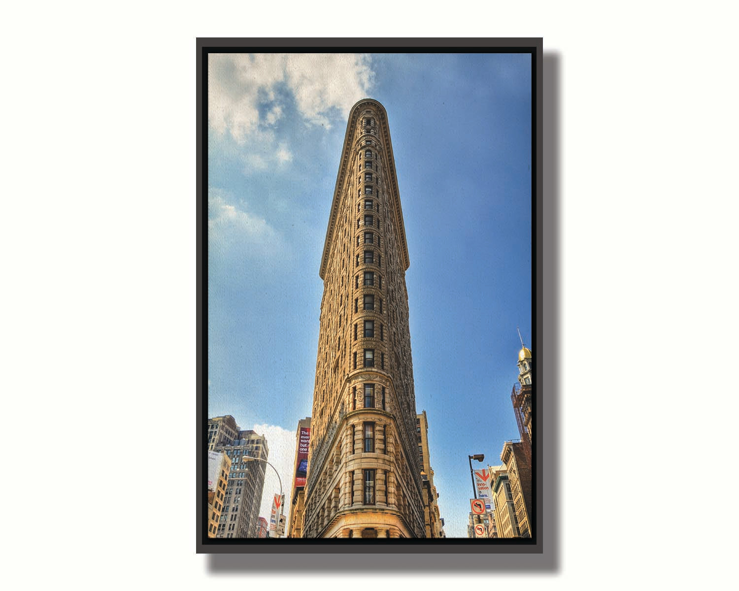 A photo of the Flatiron Building in New York City, New York. Its iconic triangular shape is captures against a bright blue sky. Printed on canvas in a float frame.