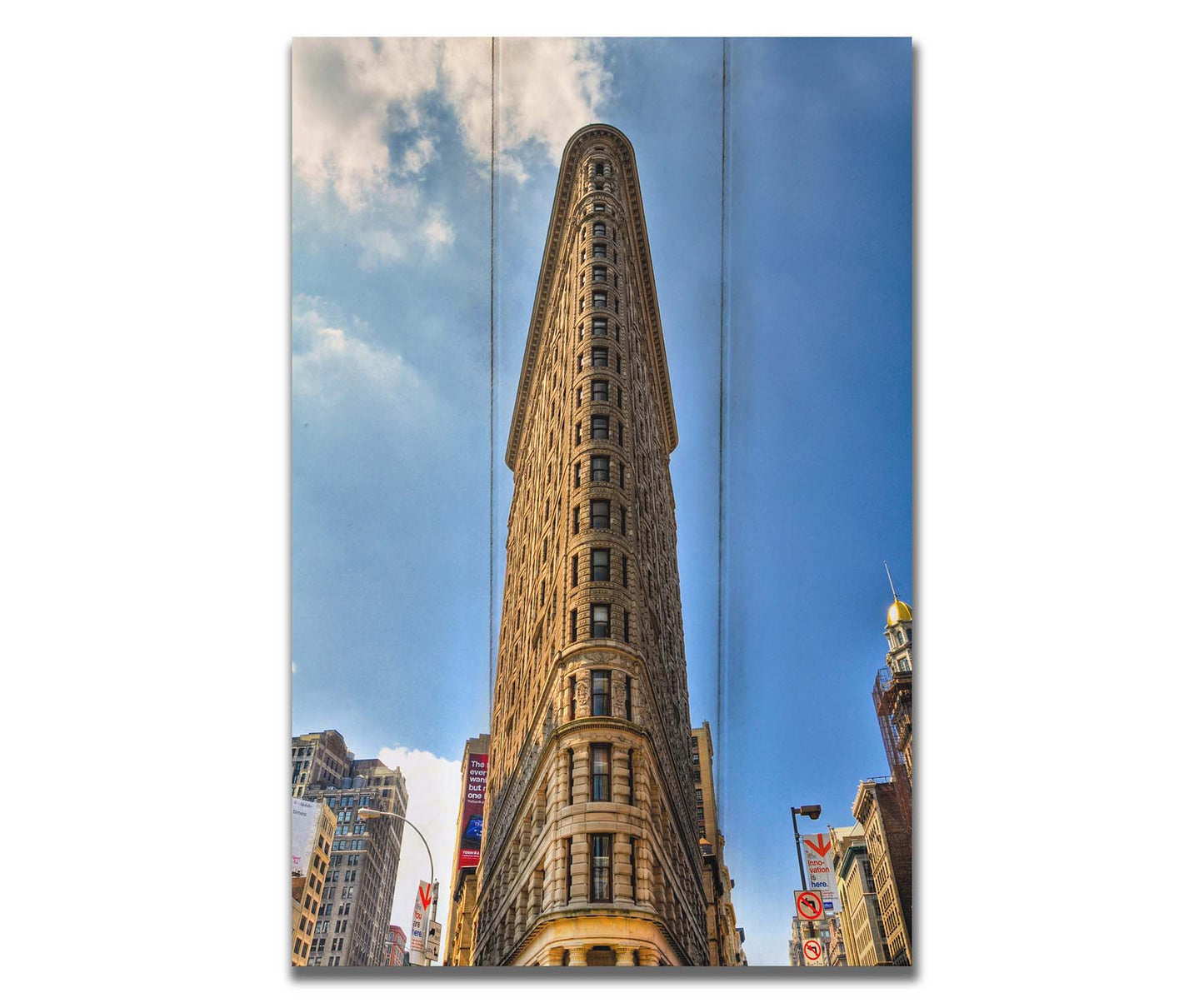 A photo of the Flatiron Building in New York City, New York. Its iconic triangular shape is captures against a bright blue sky. Printed on a box board.