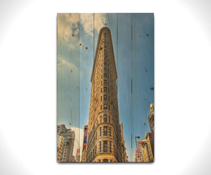 A photo of the Flatiron Building in New York City, New York. Its iconic triangular shape is captures against a bright blue sky. Printed on a wood pallet.