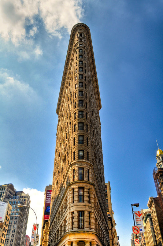 A photo of the Flatiron Building in New York City, New York. Its iconic triangular shape is captures against a bright blue sky.
