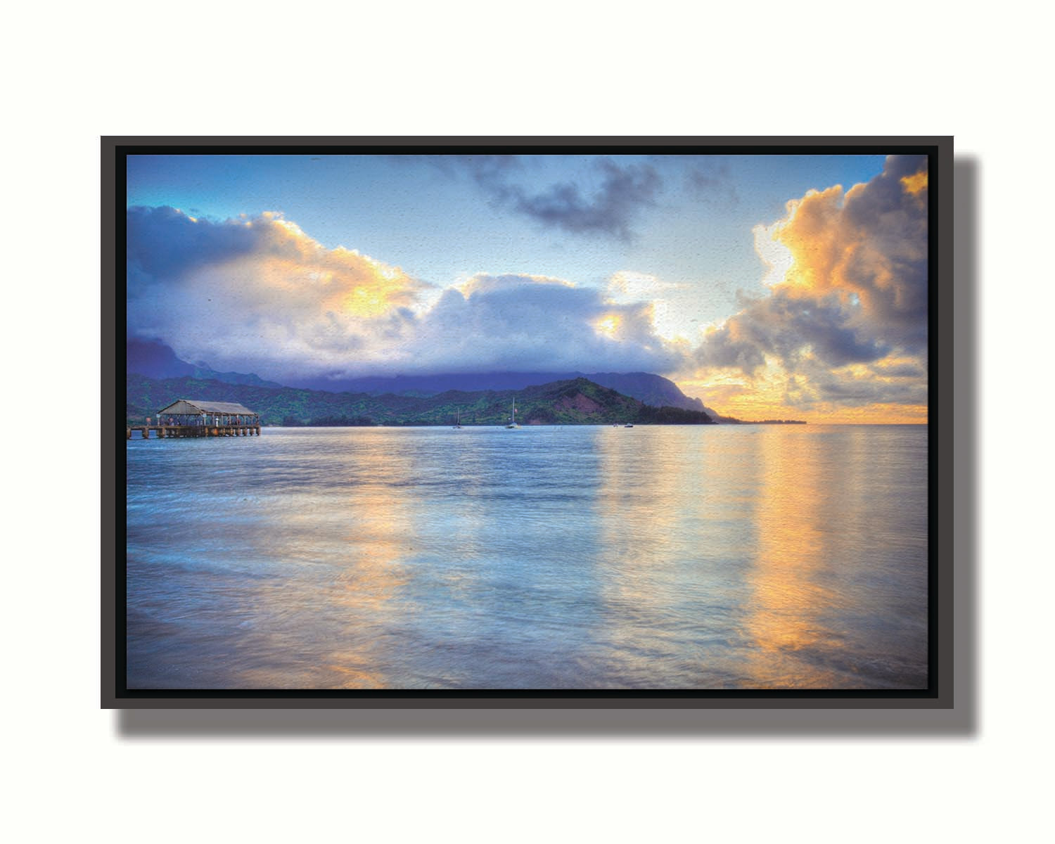 A photo of the ocean at Hanalei Bay at sunset. Clouds rest atop the mountains and reflect the golden light. Printed on canvas in a float frame.