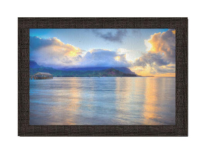 A photo of the ocean at Hanalei Bay at sunset. Clouds rest atop the mountains and reflect the golden light. Printed on canvas and framed.