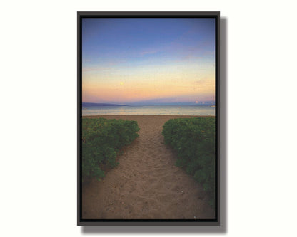 A photo looking out to sea at Kaʻanapali beach at sunset. Lush foliage lines the path down the beach, and sail boats can be see on the water. Printed on canvas in a float frame.