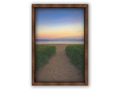 A photo looking out to sea at Kaʻanapali beach at sunset. Lush foliage lines the path down the beach, and sail boats can be see on the water. Printed on canvas and framed.