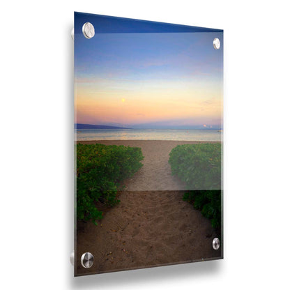 A photo looking out to sea at Kaʻanapali beach at sunset. Lush foliage lines the path down the beach, and sail boats can be see on the water. Printed on acrylic.