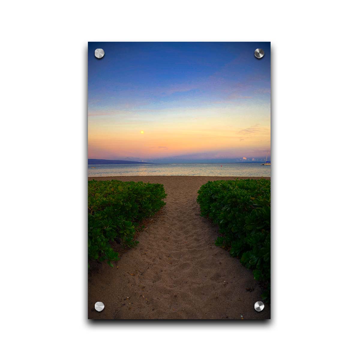 A photo looking out to sea at Kaʻanapali beach at sunset. Lush foliage lines the path down the beach, and sail boats can be see on the water. Printed on acrylic.