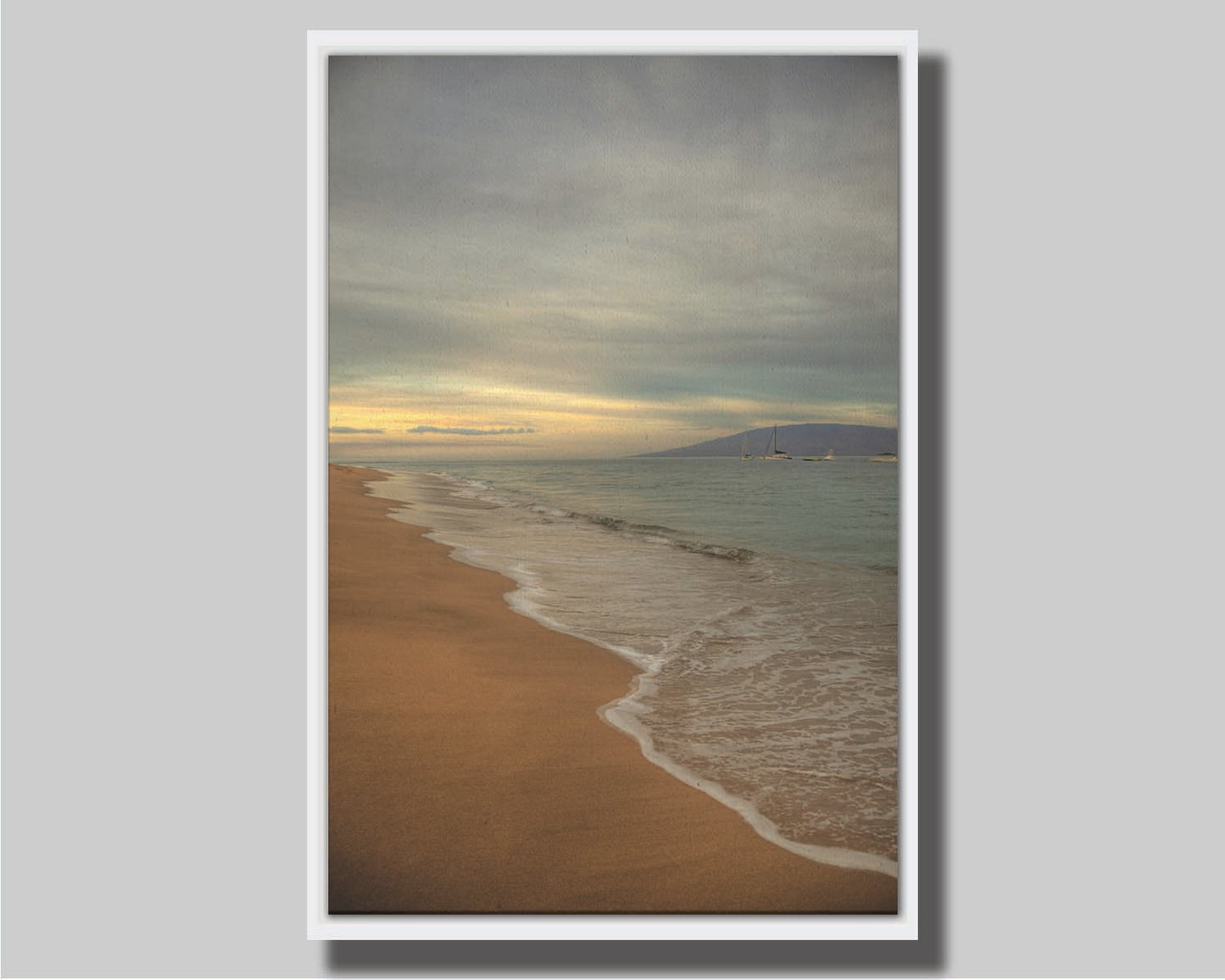 A photo of a cloudy sunrise on the Kaʻanapali shore, looking out to sea. Sailboats can be seen out on the water. Printed on canvas in a float frame.