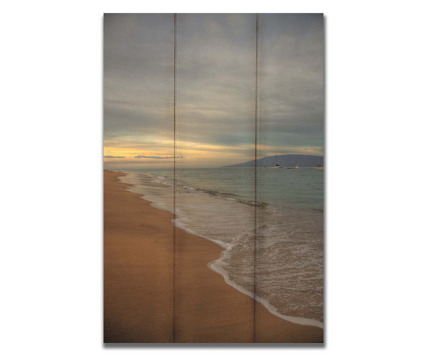 A photo of a cloudy sunrise on the Kaʻanapali shore, looking out to sea. Sailboats can be seen out on the water. Printed on a box board.