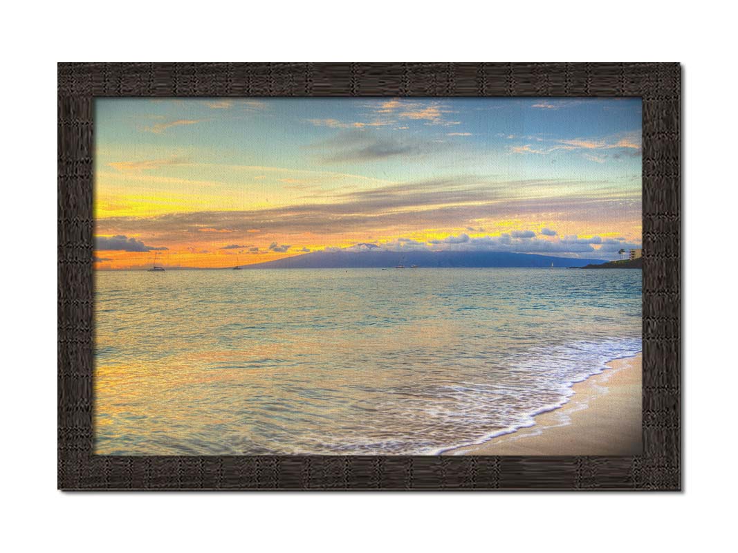 A photo of the sunset on the beach at Kaʻanapali, looking out to sea. Sailboats can be seen on the water, and mountains stand tall among clouds in the background. Printed on canvas and framed.