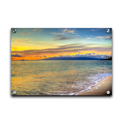 A photo of the sunset on the beach at Kaʻanapali, looking out to sea. Sailboats can be seen on the water, and mountains stand tall among clouds in the background. Printed on acrylic.