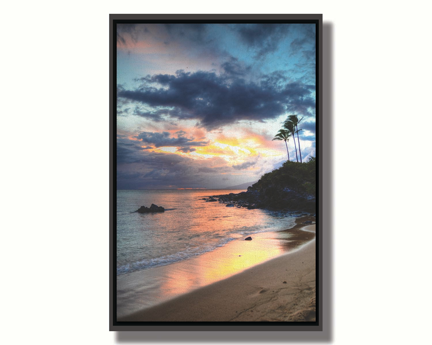 A photo of the sunset at Honokahua, Maui peeking through the clouds and reflecting pink and orange on the water. Palms are silhouetted against the sky. Printed on canvas in a float frame.