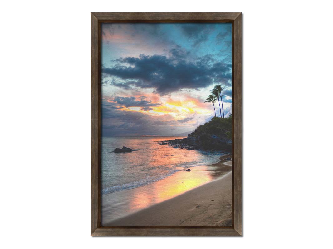 A photo of the sunset at Honokahua, Maui peeking through the clouds and reflecting pink and orange on the water. Palms are silhouetted against the sky. Printed on canvas and framed.