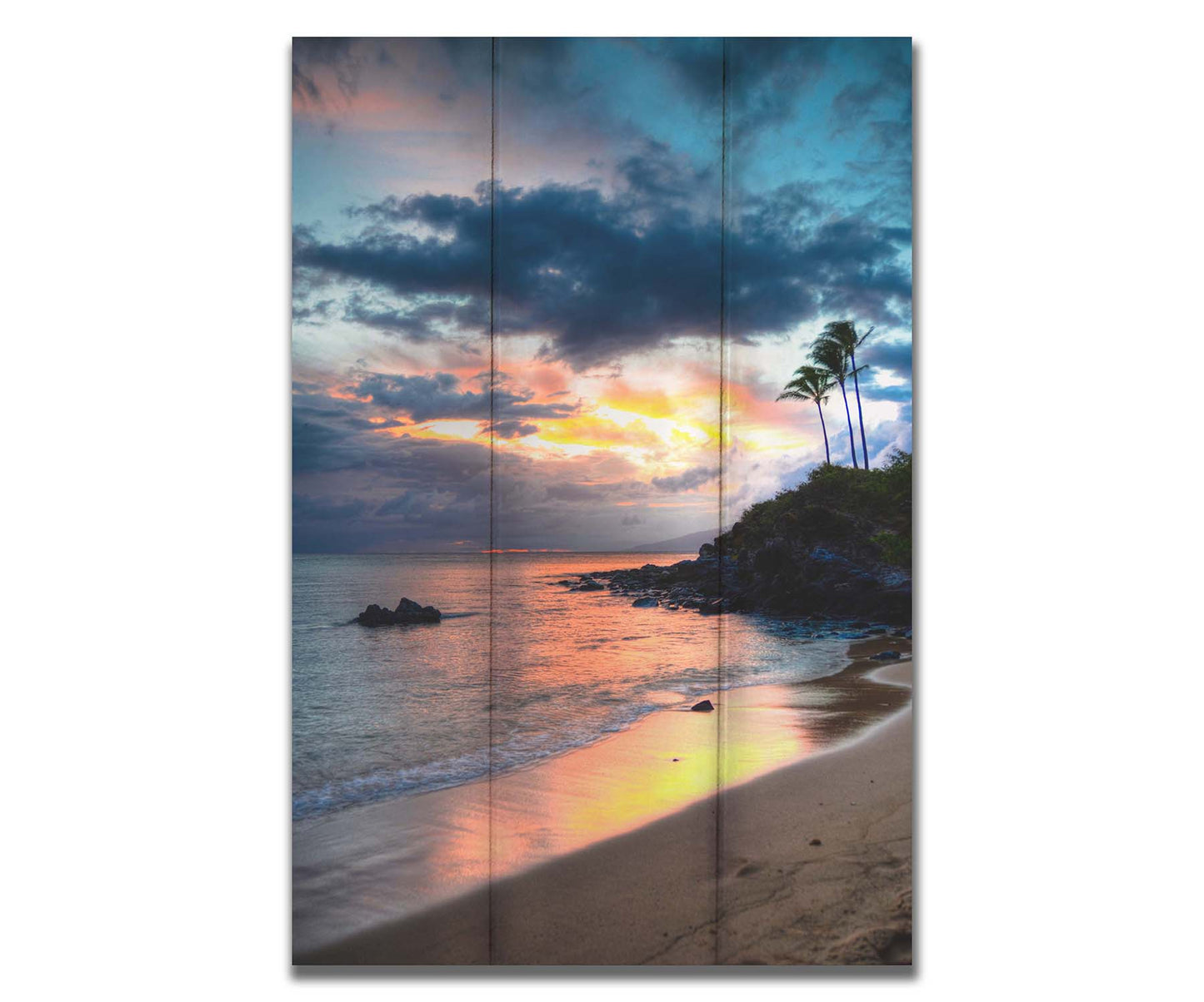 A photo of the sunset at Honokahua, Maui peeking through the clouds and reflecting pink and orange on the water. Palms are silhouetted against the sky. Printed on a box board.