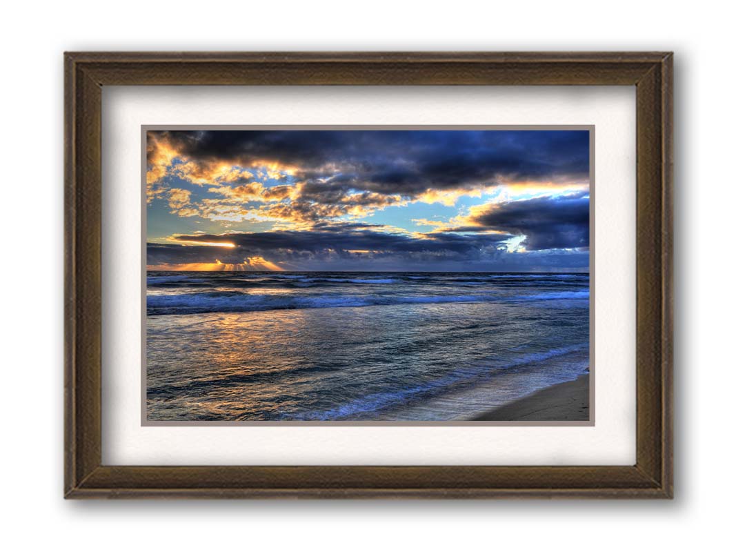 A photo looking out to sea off the coast of Kauaʻi at sunrise. The sunlight reflects off the sea and clouds in a beautiful parallel. Printed on paper, matted, and framed.