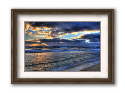 A photo looking out to sea off the coast of Kauaʻi at sunrise. The sunlight reflects off the sea and clouds in a beautiful parallel. Printed on paper, matted, and framed.