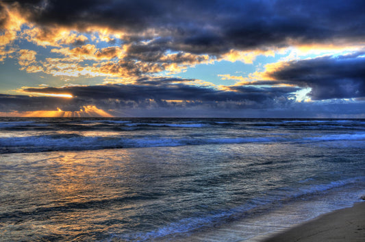 A photo looking out to sea off the coast of Kauaʻi at sunrise. The sunlight reflects off the sea and clouds in a beautiful parallel.