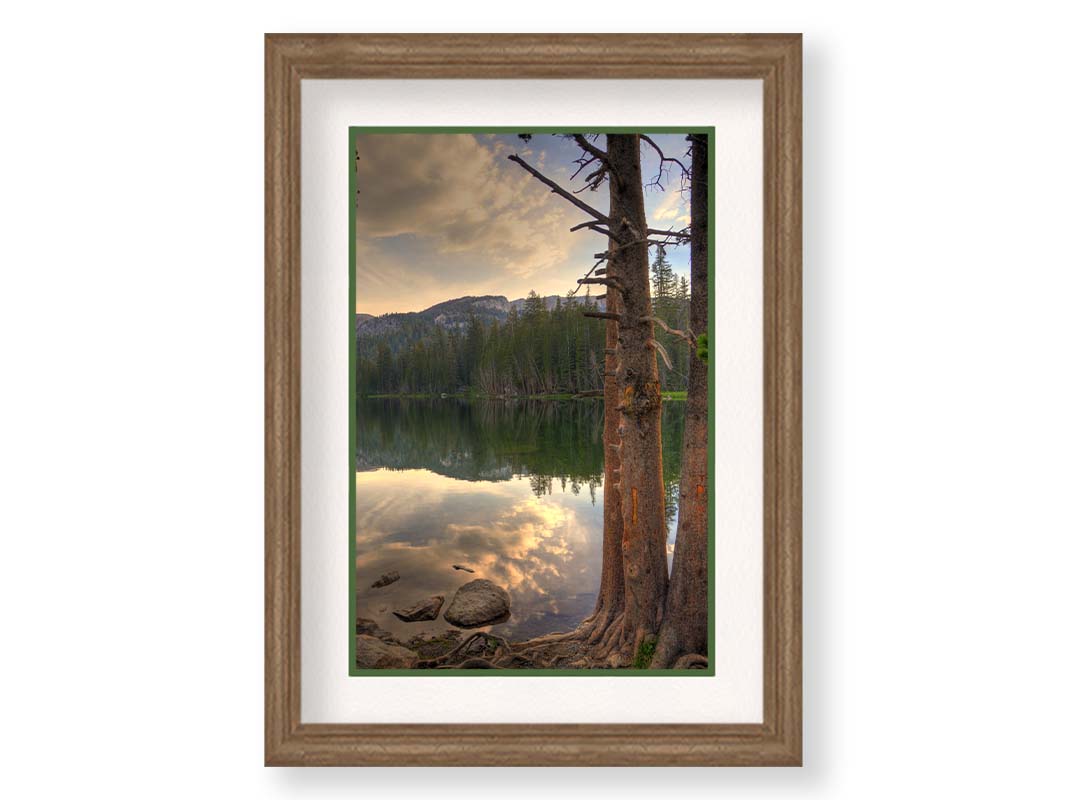 A photo overlooking Lake Mamie at Mammoth Mountain, California. The lake is surrounded by a forest of trees, with the mountains in the background. Printed on paper, matted, and framed.