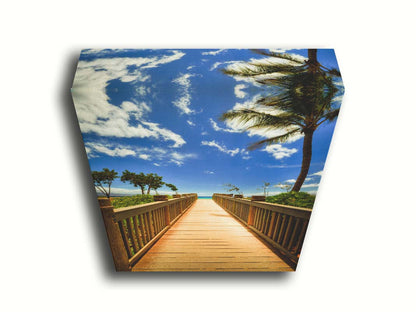 A photo of a boardwalk in Maui, Hawaiʻi, looking down the wood path to the sea. It is flanked by shrubbery, palms, and other tropical trees. Printed on canvas.